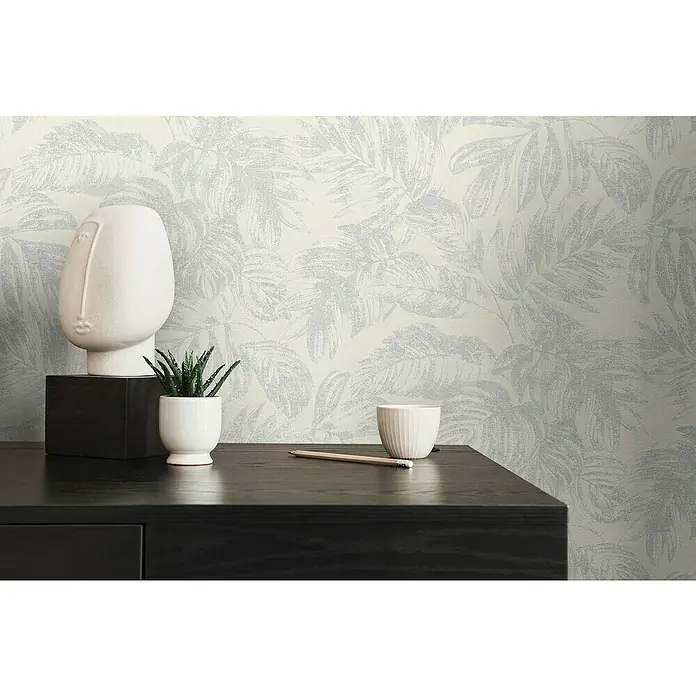 A.S. Création Casual Living Vliestapete - Weiß/Silber/Creme, Floral, 10,05 x 0,53 m - Nahaufnahme eines Schreibtischs mit Dekorationsgegenständen vor einer Blättertapete.