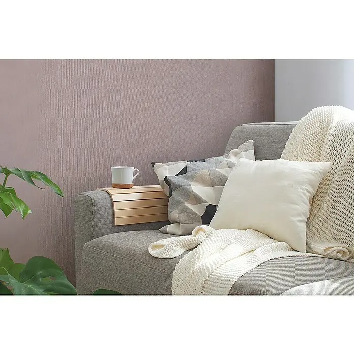 A.S. Création Casual Living Vliestapete Strukturtapete - Rosa/Silber, Uni, 10,05 x 0,53 m - Nahaufnahme eines Sofas mit Kissen und einer Tasse, die auf einem Holztablett steht. Die Textur der Wand verleiht dem Bild Tiefe.