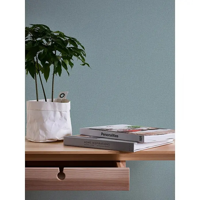 A.S. Création Casual Living Vliestapete Textilstruktur - Türkis, Uni, 10,05 x 0,53 m - Nahaufnahme von zwei Büchern, einer Zimmerpflanze und einer Holzkommode, die eine gemütliche und einladende Atmosphäre vermitteln.