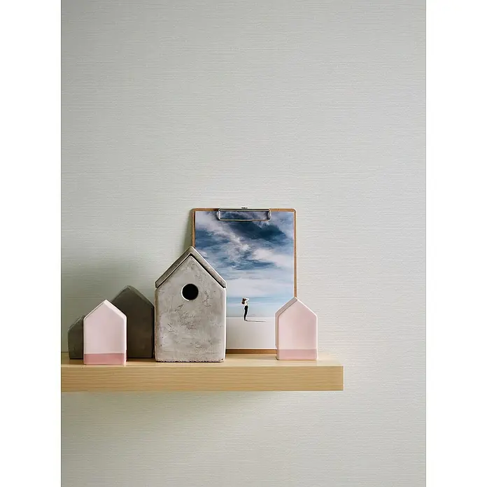 A.S. Création Casual Living Vliestapete - Strukturweiß, Uni, 10,05 x 0,53 m - Regal mit Deko-Häusern und einem Bild mit einem bewölkten Himmel. Die Häuser haben verschiedene Farben und Materialien.