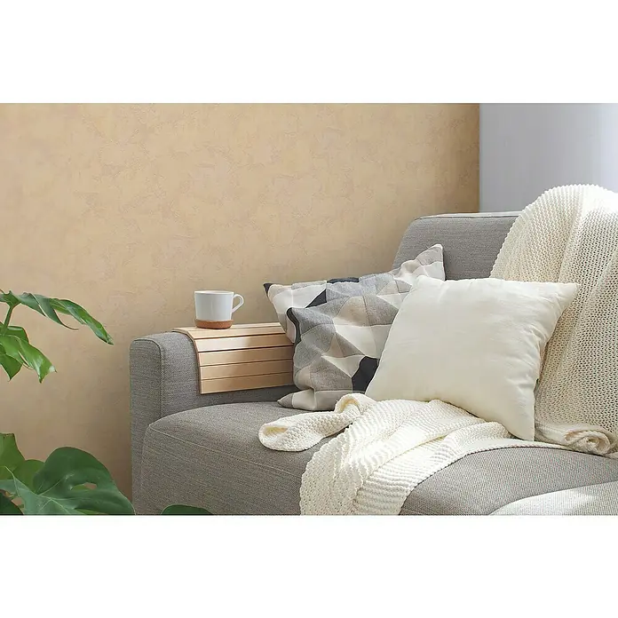 A.S. Création Casual Living Vliestapete - Beige, Uni, 10,05 x 0,53 m - Gemütliche Couch-Szene mit Kaffeetasse, Kissen und Strickdecke. Die Holzablage auf der Armlehne bietet eine praktische Ablagefläche.