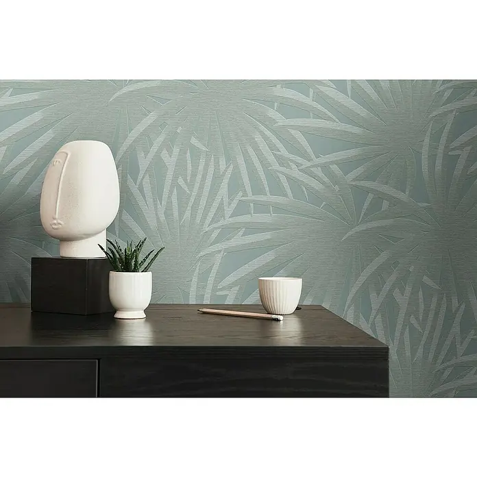 A.S. Création Casual Living Vliestapete Palmenblätter - Blau/Mint, Floral, 10,05 x 0,53 m - Dekorative Inneneinrichtung mit einer abstrakten Kopfskulptur, einer Sukkulente und einem Stift auf einer dunklen Kommode vor einer blauen Tapete.