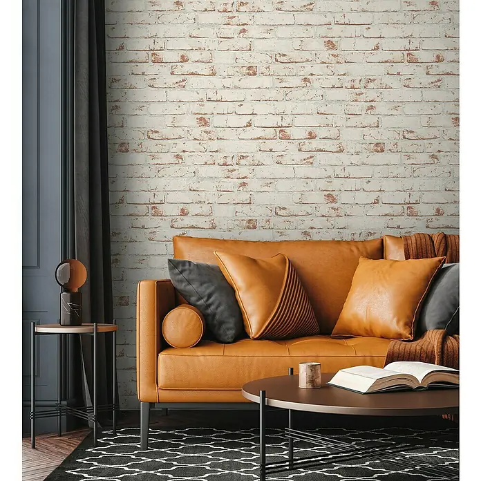 A.S. Création Casual Living Vliestapete New England Klinker - Weiß/Rot, Steinoptik, 10,05 x 0,53 m - Nahaufnahme eines stilvollen Wohnzimmers mit einem Ledersofa, Kissen und einem Beistelltisch.