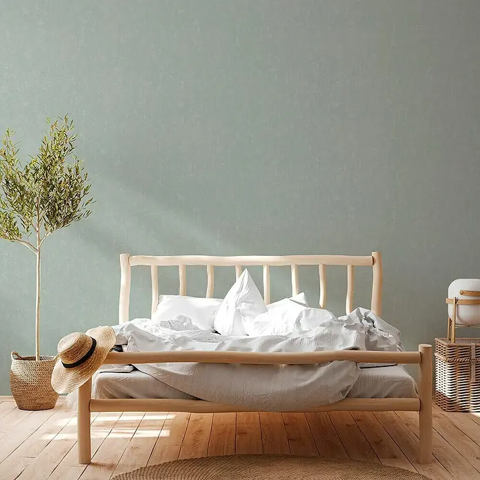 A.S. Création Casual Living Vliestapete - Mintblau, Uni, 10,05 x 0,53 m - Ein helles Holzbett mit weißer Bettwäsche und einem Strohhut im Schlafzimmer, ergänzt durch einen grünen Olivenbaum im Korb und einen Teppich.