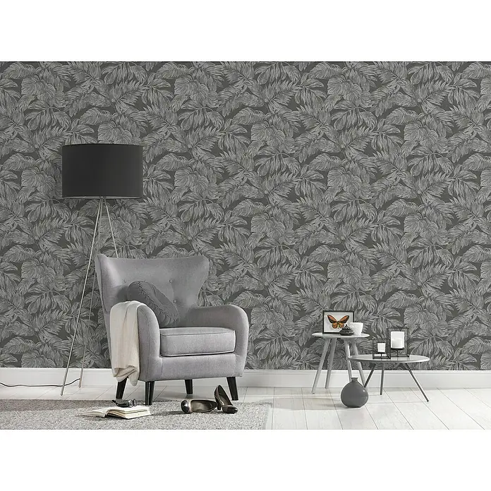 A.S. Création Casual Living Vliestapete - Anthrazit/Grau/Silber, Floral, 10,05 x 0,53 m - Elegantes Interieur mit grauem Sessel, Stehlampe und Beistelltischen vor einer dunklen Blättertapete. Stilvolle Wohnraumgestaltung.