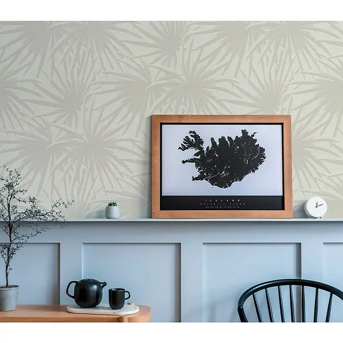 A.S. Création Casual Living Vliestapete Palmenblätter - Creme/Hellgrau, Floral, 10,05 x 0,53 m - Stillleben mit Island-Poster im Holzrahmen, Teekanne und Tasse auf einem Beistelltisch, vor einer Wand mit Blattmuster.