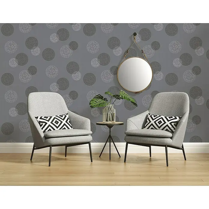 A.S. Création Casual Living Vliestapete Kreise - Anthrazitgrau, Grafisch, 10,05 x 0,53 m - Zwei graue Sessel mit einem kleinen Beistelltisch und einem runden Spiegel vor einer Wand mit einem grauen Punktmuster.