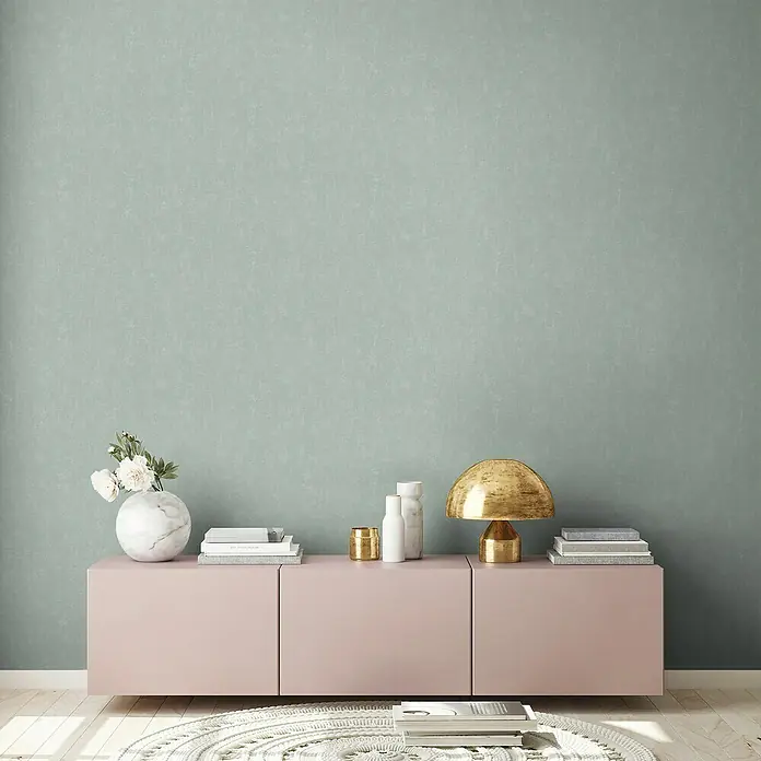 A.S. Création Casual Living Vliestapete - Mintblau, Uni, 10,05 x 0,53 m - Ein stilvolles Interieur mit einem Sideboard in zartem Rosa, dekoriert mit Vasen, Büchern und einer goldenen Lampe vor einer sanft grünen Wand.