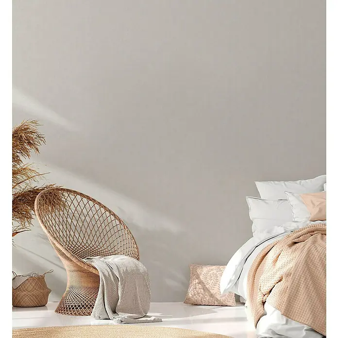 A.S. Création Casual Living Vliestapete - Grau/Hellgrau, Uni, 10,05 x 0,53 m - Gemütliches Interieur mit Rattan-Stuhl, Decken und Kissen in sanften Farben, die eine entspannte Atmosphäre schaffen.