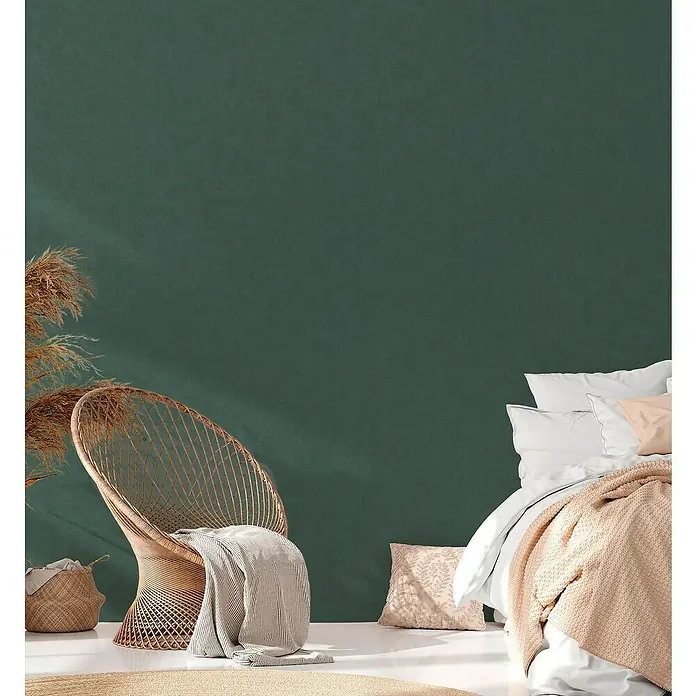 A.S. Création Casual Living Vliestapete - Grün, Uni, 10,05 x 0,53 m - Einrichtungsidee mit Rattansessel, Korb und Textilien in sanften Farbtönen vor einer grünen Wand. Gemütliche Atmosphäre.