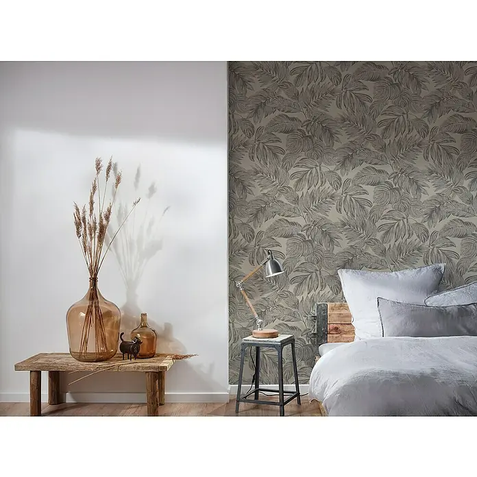 A.S. Création Casual Living Vliestapete - Braun/Grau/Beige, Floral, 10,05 x 0,53 m - Einrichten Sie Ihr Schlafzimmer mit einer dezenten Blättertapete, einem Holztisch mit Glasvasen und einer Lampe für eine warme Atmosphäre.