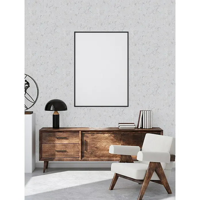 A.S. Création Casual Living Vliestapete Struktur - Grau/Silber/Metallic, Uni, 10,05 x 0,53 m - Ein stilvolles Wohnzimmer mit einem weißen Sessel, einer Holzkommode und einem gerahmten Bild an der Wand, das eine moderne und elegante Atmosphäre schafft.