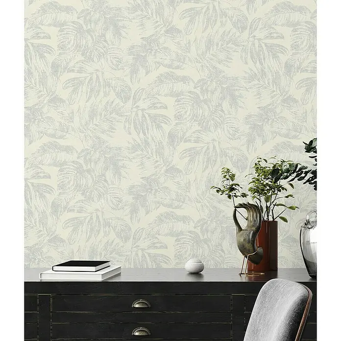 A.S. Création Casual Living Vliestapete - Weiß/Silber/Creme, Floral, 10,05 x 0,53 m - Ein elegantes Interieur mit einer stilvollen Kommode und einer dezenten Tapete mit Blattmuster, die dem Raum eine ruhige Atmosphäre verleiht.