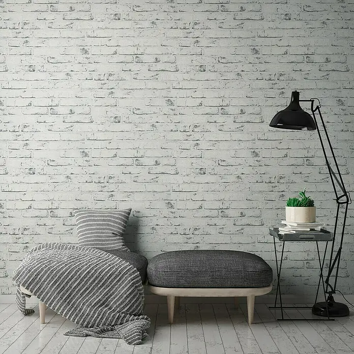 A.S. Création Casual Living Vliestapete New England Klinker - Grau/Anthrazit, Steinoptik, 10 x 0,53 m - Elegantes Interieur mit einem stilvollen grauen Hocker und einer passenden Decke, perfekt für ein gemütliches Ambiente.