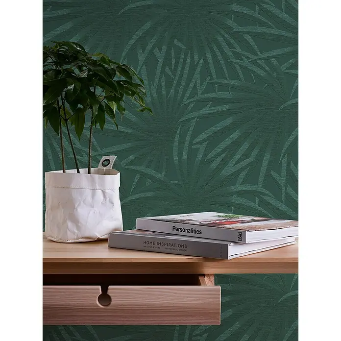 A.S. Création Casual Living Vliestapete Palmenblätter - Grün/Dunkelgrün, Floral, 10,05 x 0,53 m - Dekorative Nahaufnahme eines Schreibtisches mit Pflanze, Büchern und einer grünen Blättertapete im Hintergrund für ein gemütliches Ambiente.