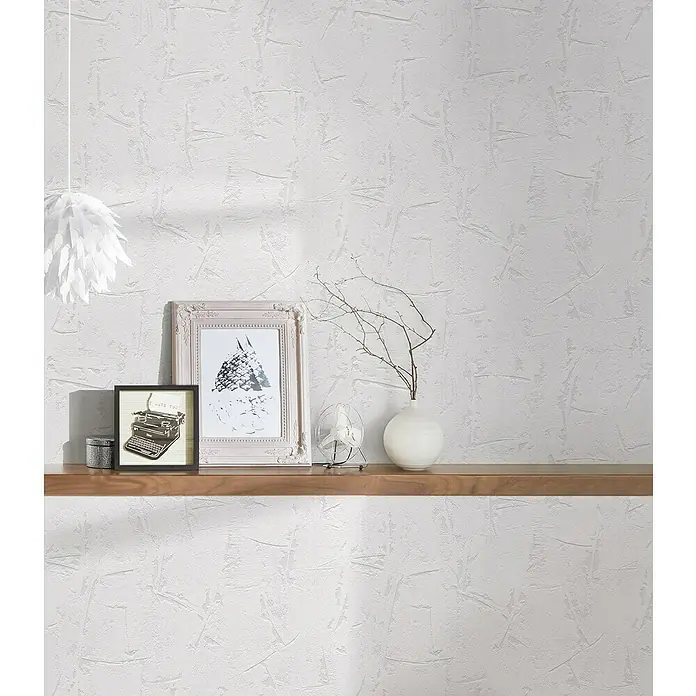 A.S. Création Casual Living Vliestapete Strukturtapete - Weiß, Uni, 10,05 x 0,53 m - Diese Nahaufnahme zeigt eine Holzwandkonsole mit dekorativen Elementen wie Bilderrahmen, einer Vase und einer Lampe vor einer strukturierten Wand.