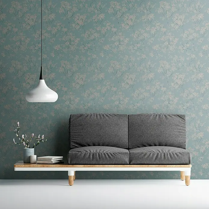 A.S. Création Casual Living Vliestapete Blümchen - Blau/Beige/Türkis, Floral, 10,05 x 0,53 m - Graues Sofa auf einer Holzbank mit weißem Rahmen und zarten weißen Blumenmustern an der Wand im Hintergrund.