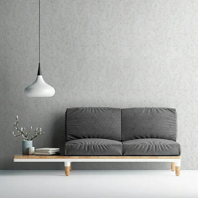 A.S. Création Casual Living Vliestapete - Hellgrau/Weiß, Floral, 10,05 x 0,53 m - Graues Sofa mit Holzrahmen und einer Lampe, die von der Decke hängt, vor einer dezent gemusterten Wand.