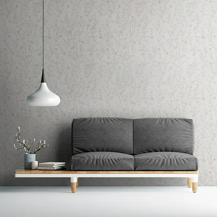 A.S. Création Casual Living Vliestapete - Hellrosa/Hellgrau, Floral, 10,05 x 0,53 m - Graues Sofa mit Bücher und Blumen in einer Vase, stilvoll präsentiert vor einer dezent gemusterten Wand und einer modernen Hängelampe.