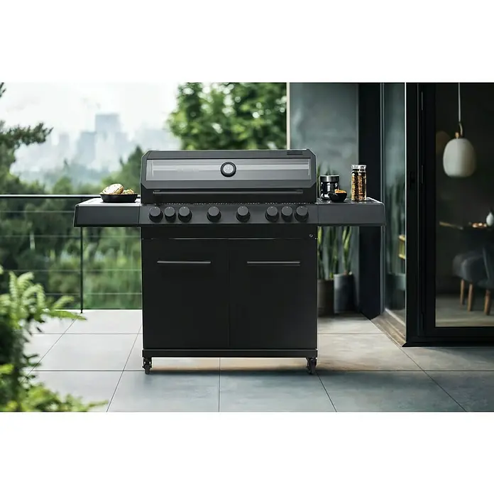 Kingstone KMS Gasgrill Cliff 6500 Beast Black Edition - Grillfläche (B x T): 90,5 x 45 cm, 21 kW, Anzahl Brenner: 6 Stk. - Schwarzer Gasgrill mit Bedienknöpfen und Seitenablage auf einer Terrasse. Im Hintergrund Grünpflanzen und eine Stadtansicht.