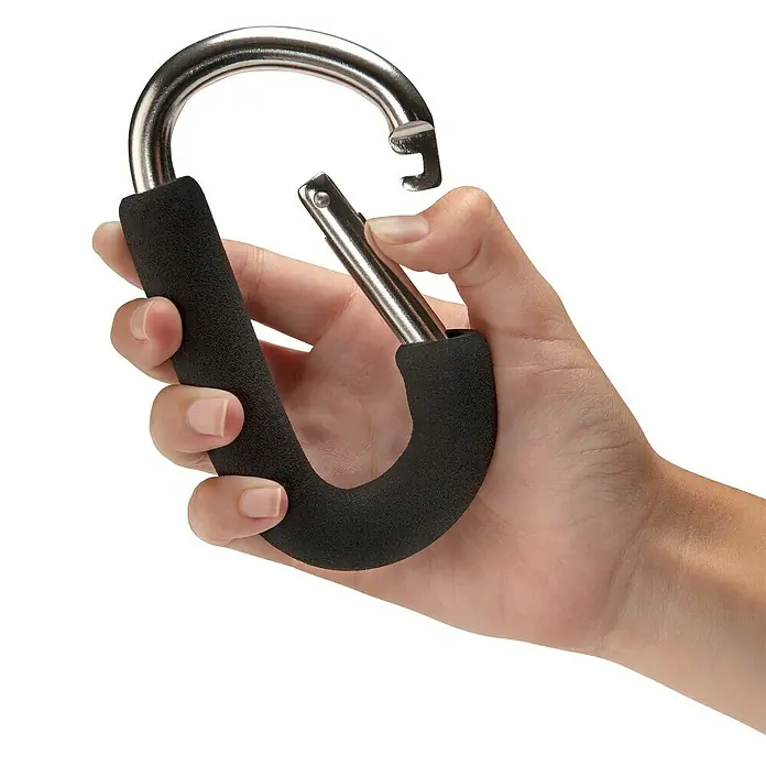 Inofix Mosquetón - Aluminio, Apto para: Cochecito de bebé, 1 ud. - Una mano sujetando un mango negro con un mosquetón. El mosquetón está abierto y está listo para sostener algo.