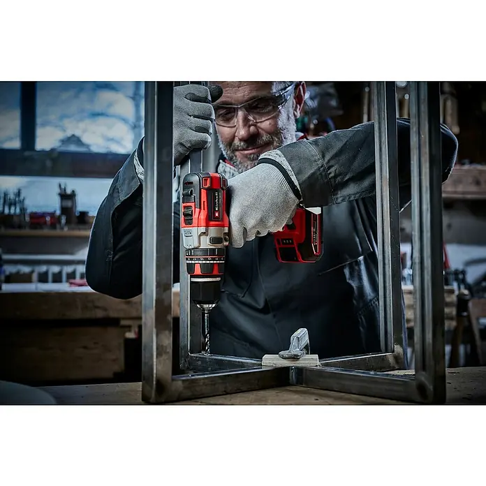 Einhell PXC 18V Taladro atornillador percutor de batería TP-CD 18/80 Li-i BL - 18 V, Sin batería, Número máx. de impactos: 28.800 /min - Un hombre usa un taladro inalámbrico Einhell para perforar un marco de metal. El taladro es rojo y gris y funciona con una batería.