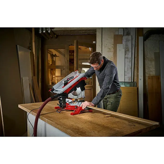 Einhell Sierra ingletadora - 2.000 W, Diámetro hoja de sierra: 254 mm, Número de revoluciones de marcha en vacío: 5.000 r.p.m. - Un hombre usa una sierra ingletadora Einhell roja y plateada para cortar un trozo de madera en un taller.