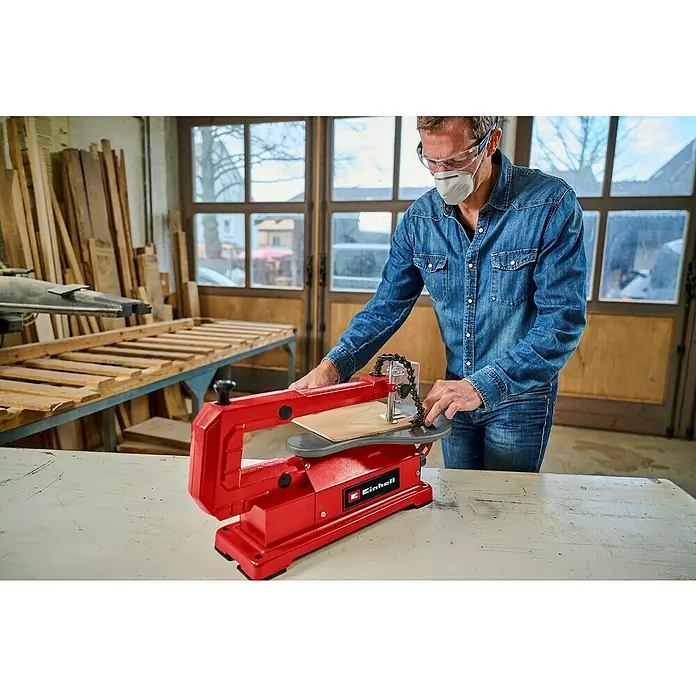 Einhell Dekupiersäge TC-SS 406 E - 120 W, 400 U/min - 1.600 U/min - Ein Mann arbeitet mit einer roten Einhell Dekupiersäge, um Holz zu schneiden. Er trägt Schutzkleidung für Augen und Atemwege in einer Werkstatt.