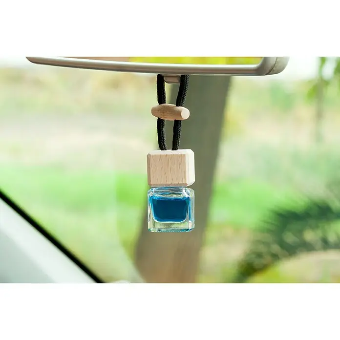 Ambientador de coche para colgar - Vainilla, 8 sem. - Un ambientador de coche en una botella de vidrio con líquido azul cuelga del espejo retrovisor de un coche. El ambientador tiene detalles de madera y una cuerda.