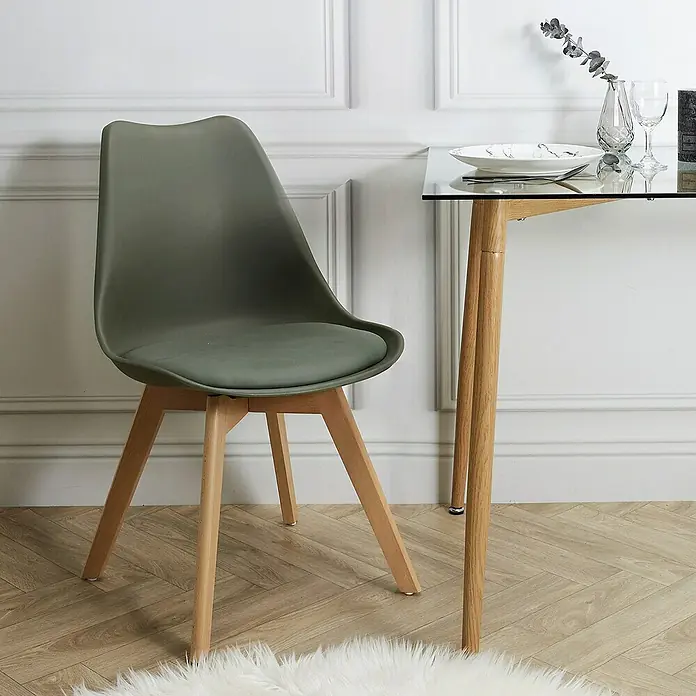 Silla Copenhague - Caqui, 4 pzs. - Una silla de color verde oliva con patas de madera se muestra junto a una mesa de sobre de vidrio con marco de madera, minimalista y moderna.