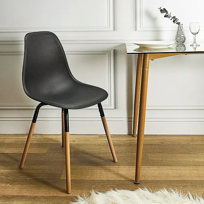 Silla Phenix - Negro, 4 pzs. - Una moderna silla negra con patas de madera se sienta junto a una mesa de vidrio, que está decorada con platos. Los muebles añaden elegancia a la habitación.