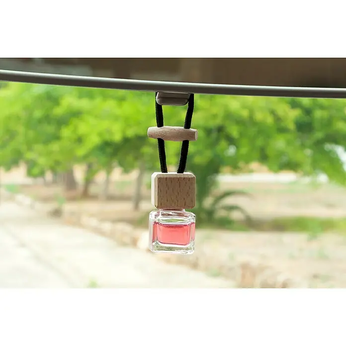 Ambientador de coche para colgar - Fresa, 8 sem. - Ambientador para coche con detalles de madera y una pequeña botella de vidrio con líquido rosa colgando de una barra.