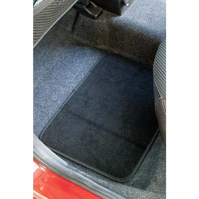 Juego de alfombrillas para coche Clasic - 4 pzs., Negro - Una alfombrilla negra para coche se encuentra sobre la moqueta gris en el espacio para los pies de un coche. La alfombra tiene un borde estrecho y oscuro.