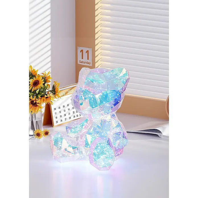 Tween Light LED-Dekoleuchte Benny - 6 W, Transparent/Irisierend, L x B x H: 28,5 x 32 x 40 cm, Benny - Nahaufnahme eines schillernden Kristallbären auf einem Tisch mit Sonnenblumen und einem Kalender.
