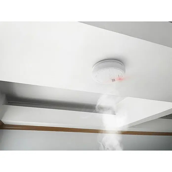 Garza Detector de humo Standart - Diámetro: 10,3 cm, Duración de batería: 5 años, Señal de alarma: 85 dB - Detector de humo en el techo con humo ascendente, enfatizando la importancia de la seguridad en el hogar.