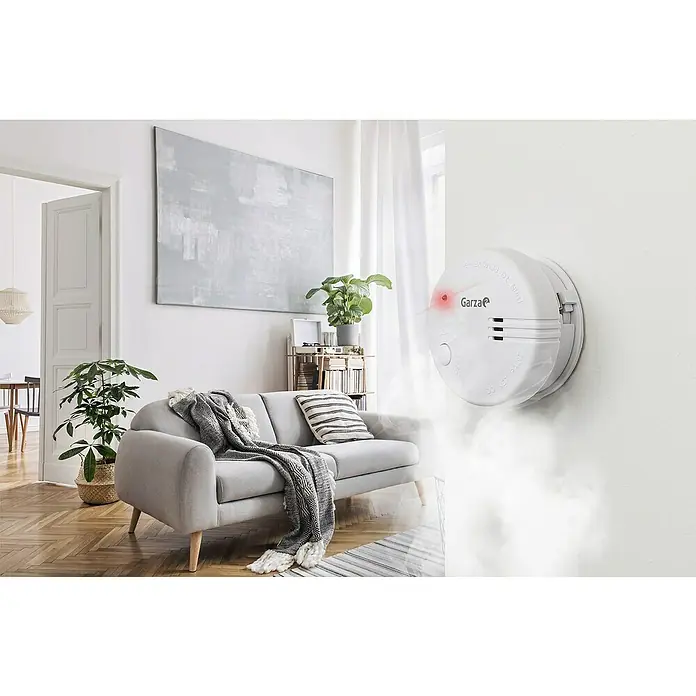 Garza Detector de humo Mini - Diámetro: 7,2 cm, Duración de batería: 5 años, Señal de alarma: 85 dB - Esta imagen muestra un detector de humo Garza en la pared, con su luz roja parpadeando para llamar la atención sobre la seguridad.