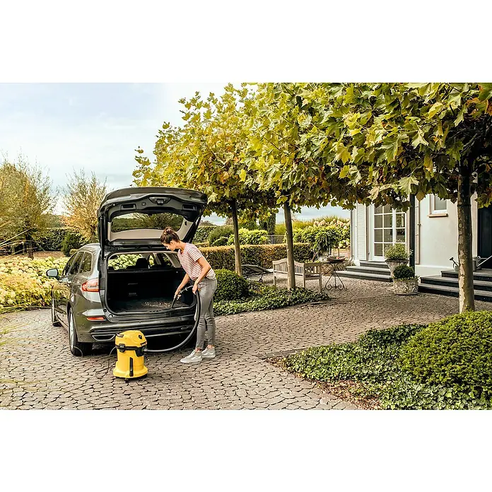 Kärcher Aspirador en seco y húmedo eléctrico WD 3 V-17/4/20 - 1.000 W, Volumen de recipiente: 17 l - Una mujer usa una aspiradora multiusos Kärcher para limpiar su coche. La aspiradora amarilla está al lado del maletero abierto del coche.