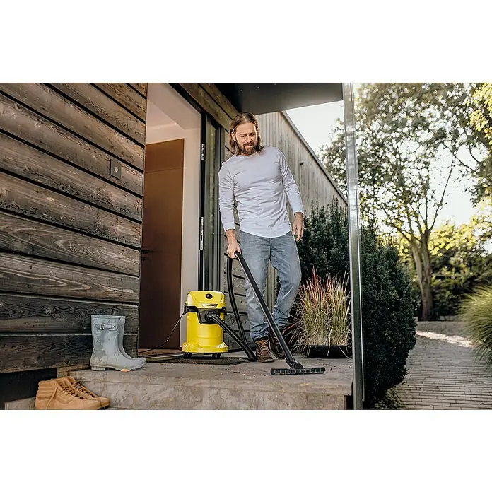 Kärcher Aspirador en seco y húmedo eléctrico WD 3 V-17/4/20 - 1.000 W, Volumen de recipiente: 17 l - Un hombre está usando una aspiradora multiusos amarilla Kärcher para limpiar un patio. Solución de limpieza práctica y versátil para exteriores.
