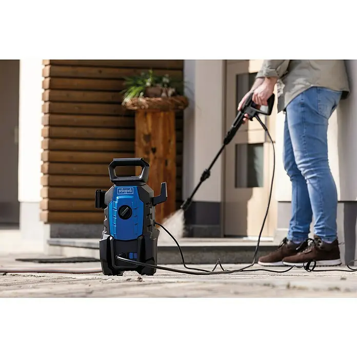 Scheppach Hidrolimpiadora de alta presión HPC1400 - 110 bar, 1.400 W, Capacidad de bombeo: 390 l/h - El limpiador de alta presión azul Scheppach está listo para la limpieza. Un hombre lo está utilizando para limpiar la acera.