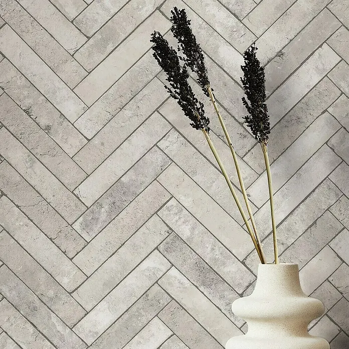 Marburg Struktura Vliestapete Fischgrat - Grau, Steinoptik, 10,05 x 0,53 m - Elegante graue Ziegelwand im Fischgrätmuster mit dekorativer Vase. Die Wandfliesen verleihen dem Raum eine moderne und stilvolle Note.