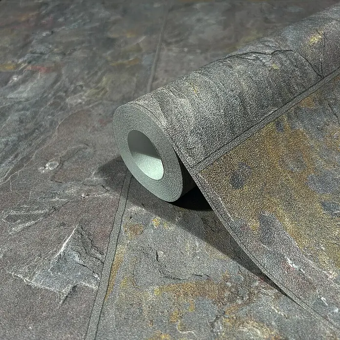 Marburg Struktura Vliestapete - Dunkelgrau, Fliesenoptik, 10,05 x 0,53 m - Nahaufnahme einer Rolle gemusterter Stein-Tapete mit dunklen und goldenen Farbtönen, die eine natürliche Optik erzeugt.