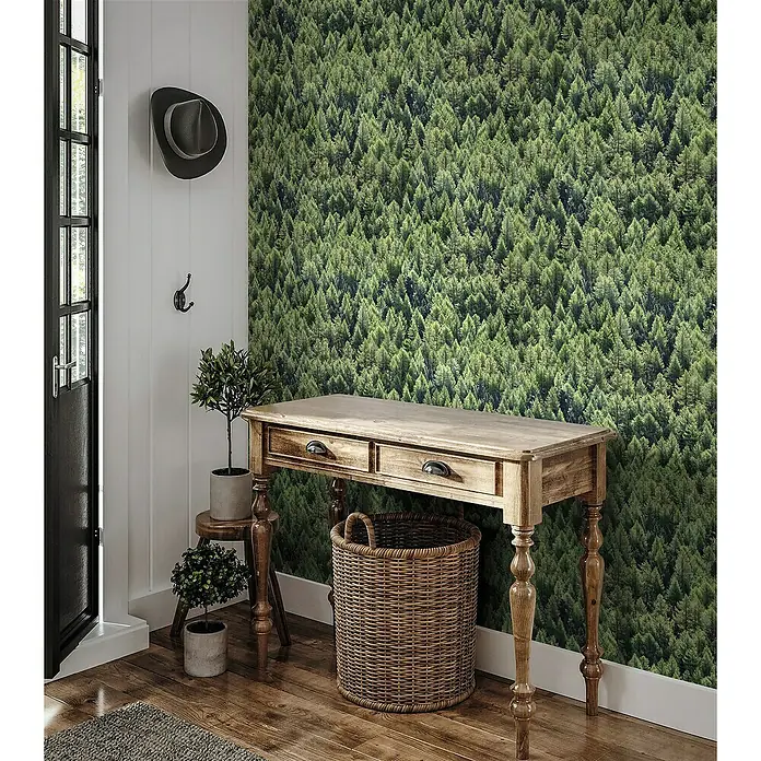 Marburg Struktura Vliestapete Nadelwald - Grün, Floral, 10,05 x 0,53 m - Detailaufnahme eines rustikalen Holzschreibtisches mit Weidenkorb und Pflanzen, vor einer grünen Waldtapete.