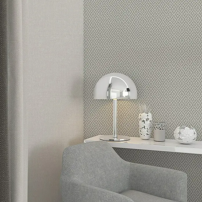 Marburg Struktura Vliestapete 3D-Rauten - Beigegrau, 3D-Optik, 10,05 x 0,53 m - Eine moderne Chrom-Tischleuchte beleuchtet einen eleganten Lesebereich mit weißem Regal und grauem Sessel vor einer gemusterten Tapete.