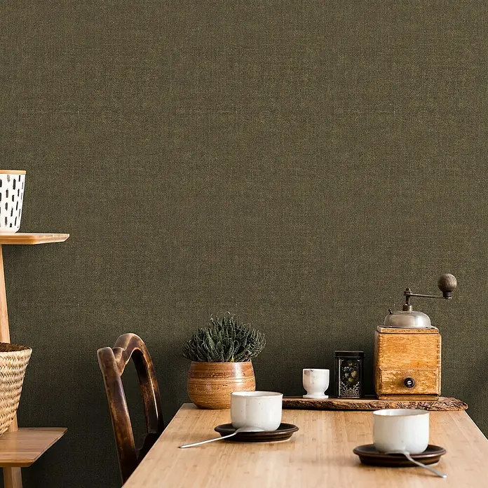 Marburg Struktura Vliestapete Struktur - Braun, Uni, 10,05 x 0,53 m - Ein rustikaler Esstisch mit Geschirr, Pflanze und Kaffeemühle vor einer strukturierten Wand.