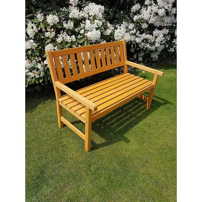 Promadino Gartenbank Johanna - B x T x H: 125 x 71 x 88,5 cm, Kiefer, Honigbraun - Eine hölzerne Gartenbank steht auf einem grünen Rasen, umgeben von blühenden Büschen. Ideal zum Entspannen im Freien.