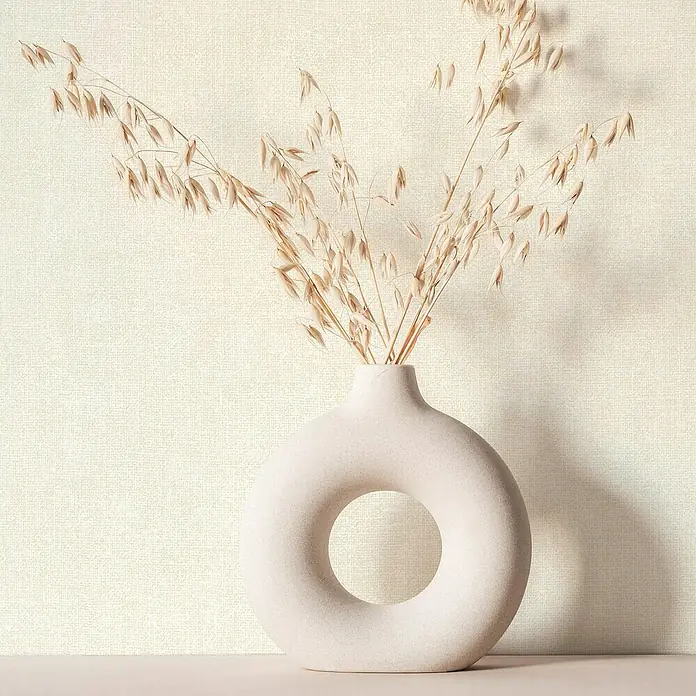 Marburg Struktura Vliestapete Struktur - Weiß, Uni, 10,05 x 0,53 m - Das Bild zeigt eine stilvolle, donut-förmige Vase mit getrocknetem Gras auf einem beigen Hintergrund.