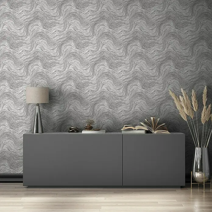 Marburg Struktura Vliestapete Marmoroptik - Grau, Steinoptik, 10,05 x 0,53 m - Elegantes graues Sideboard mit Lampe, Dekoration und Vasen auf hellem Holzboden vor einer strukturierten grauen Wand.