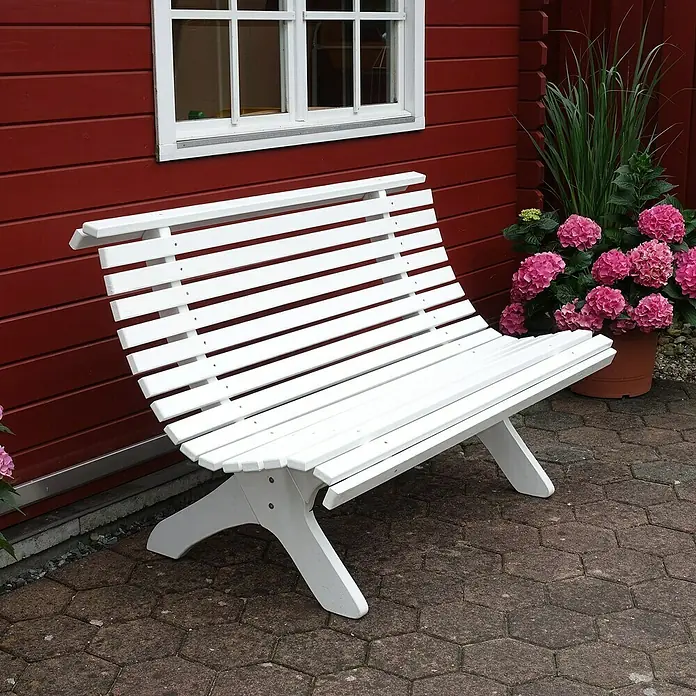 Promadino Gartenbank Sven - B x T x H: 140 x 74 x 91 cm, Kiefer, Weiß - Eine weiße Gartenbank aus Holz steht vor einer roten Holzwand mit Fenster, daneben ein Topf mit rosa Hortensien.