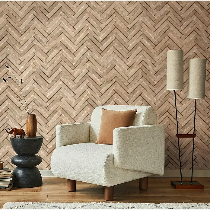 Marburg Struktura Vliestapete Fischgrät - Beige, Steinoptik, 10,05 x 0,53 m - Elegantes Interieur mit einem cremefarbenen Sessel mit braunem Kissen, stilvoller Stehlampe und dekorativem Beistelltisch vor einer Ziegelwand.