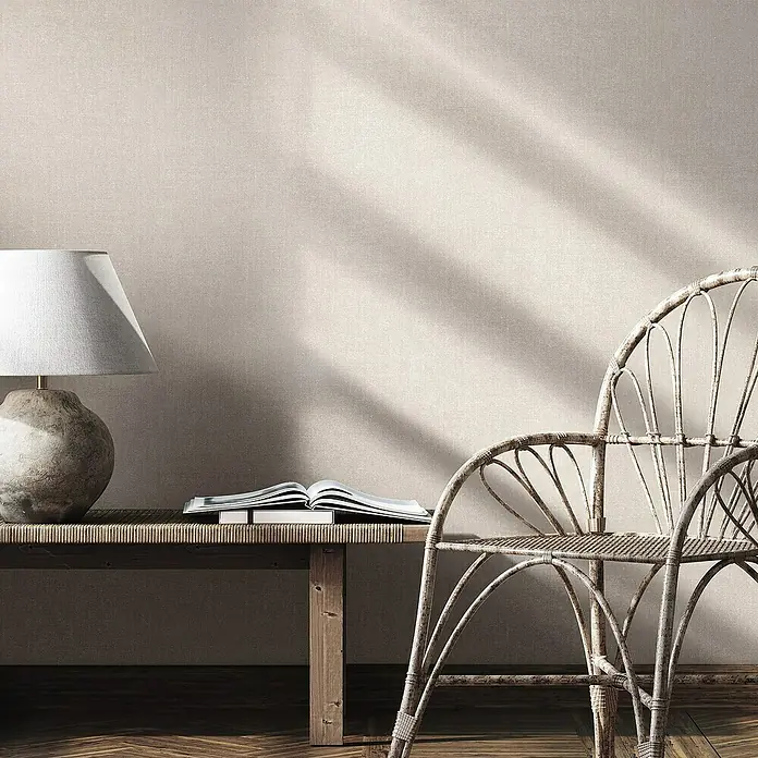 Marburg Struktura Vliestapete Struktur - Grau/Beige, Uni, 10,05 x 0,53 m - Eine elegante Szene mit einer Lampe, einem Buch auf einem Holztisch und einem dekorativen Stuhl vor einer strukturierten Wand.